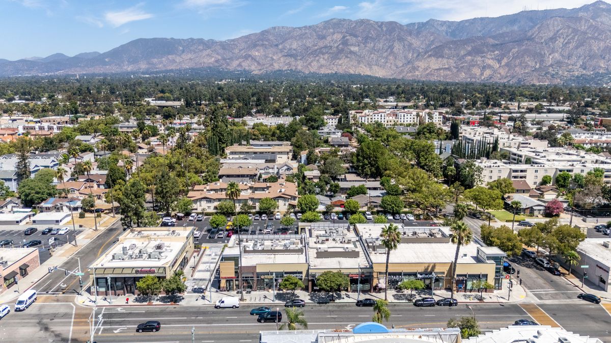 Wide aerial view of Campus Village from above Colorado Boulevard showing both buildings, the parking lot behind them, and the mountains.